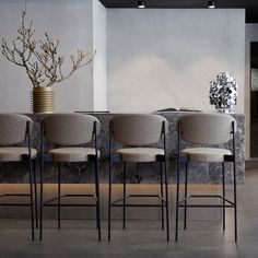 four chairs are lined up in front of a table with a vase and flowers on it