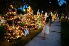 a woman walking down a sidewalk next to christmas trees covered in lights and decorations at night