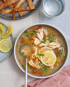 a bowl of soup with lemons, chicken and parsley next to some pita chips