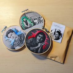 three embroidered hoops with pictures of people on them sitting on a table next to a pair of scissors