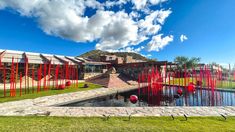 a building with red sculptures in front of it on the side of a lake and grass area