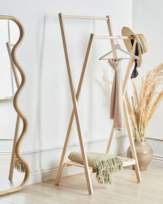 a wooden rack with clothes and hats on it next to a vase filled with dried grass