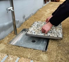 a person is placing gravel in a drain on the ground next to a metal pole