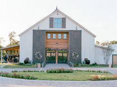 a large white barn with flowers and greenery on the front lawn is surrounded by people