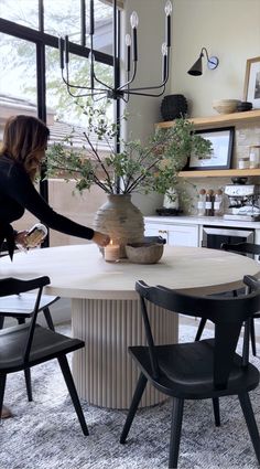 a woman standing in front of a table with chairs and a vase filled with flowers