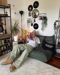 a man sitting on top of a green couch next to a wall filled with records