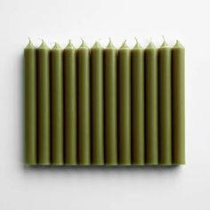 six green candles lined up against a white wall