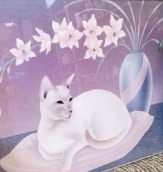 a white cat sitting on top of a rug next to a vase with flowers in it