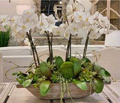 a wooden bowl filled with white flowers and greenery on top of a wood table