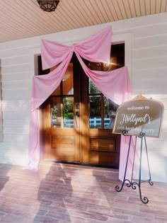 a welcome sign in front of a wooden door with pink drapes on the side