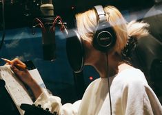 a woman wearing headphones writing on a piece of paper in front of a microphone