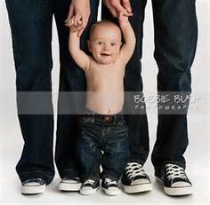 an adult holding the hand of a baby while standing next to two adults'legs