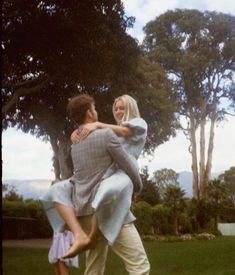 a man carrying a woman on his back in a park with trees and grass behind him