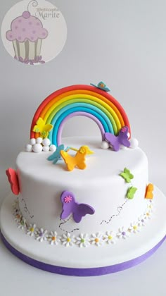 there is a white cake with rainbow decorations on the top and bottom, along with butterflies