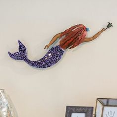 there is a mermaid statue on the wall next to a clock and other decor items