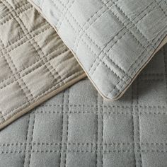 two pillows sitting next to each other on top of a bed covered in gray and white quilts