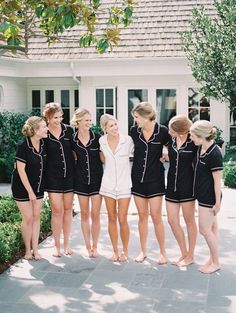 a group of women standing next to each other in front of a white house on a sunny day