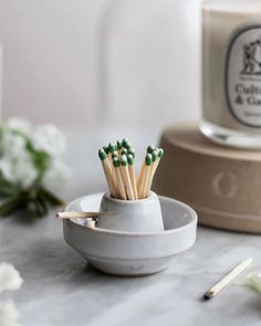 several matchsticks in a white cup on a marble table next to some flowers