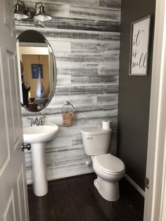 a white toilet sitting next to a sink in a bathroom under a large round mirror