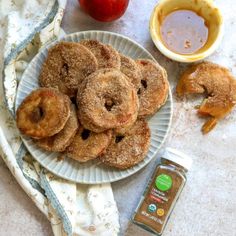 donuts are on a plate next to an apple and some dipping sauce for them