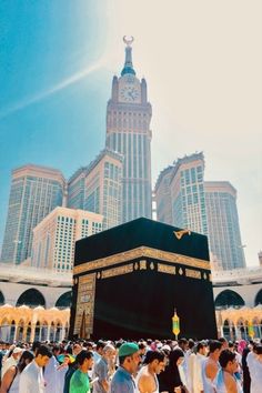 many people are standing around the kabab in front of tall buildings with a clock on it