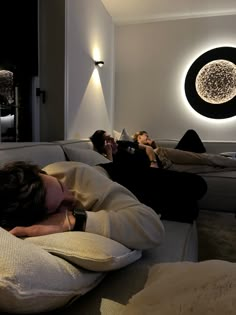 two people laying on couches in a room with white walls and black circular lights