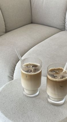 two glasses filled with liquid sitting on top of a white table next to a couch