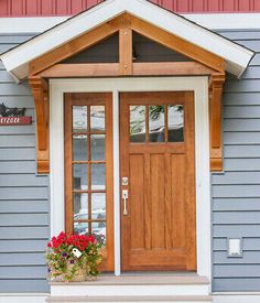 the front door of a gray house with red and white flowers