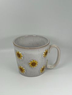 a white and yellow coffee cup with sunflowers painted on the outside of it