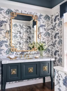 a bathroom with blue and white wallpaper, two sinks and a gold framed mirror