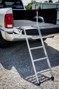 a truck with a ladder attached to the back of it's bed in gravel