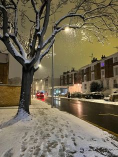 a snowy street at night with cars parked on the side and trees covered in snow