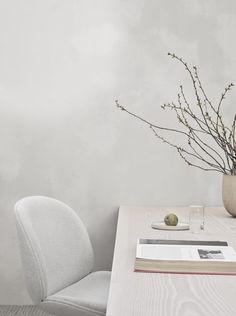 a white table with a book and vase on it, next to a gray chair