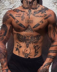 a man with lots of tattoos on his body and chest is standing in front of a wall