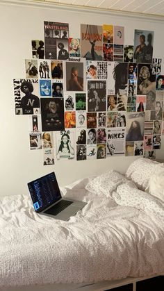 a laptop computer sitting on top of a bed covered in pictures and posters next to a white comforter