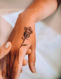 two people holding hands with tattoos on their fingers and one has a rose tattooed on it