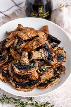 a white bowl filled with mushrooms next to a bottle of wine