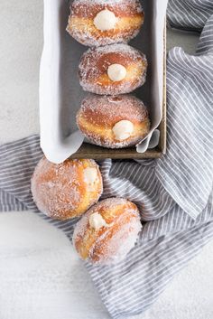 powdered sugar covered donuts in a box on top of a blue and white towel