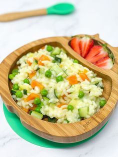 a wooden bowl filled with rice, peas and strawberries next to two spoons