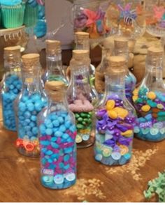 several bottles filled with candy sitting on top of a table next to cupcakes