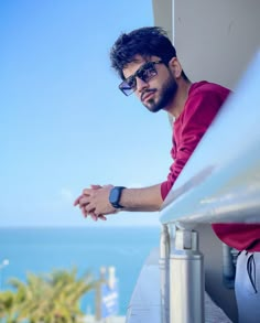 a man wearing sunglasses sitting on a ledge next to the ocean