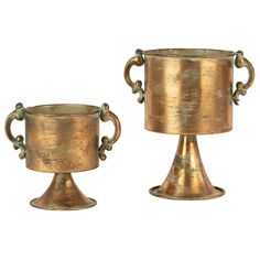 two brass vases sitting next to each other on a white background, one is holding a cup and the other has a handle