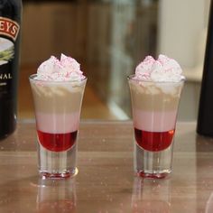 two shot glasses filled with liquid and whipped cream on a table next to a bottle of booze