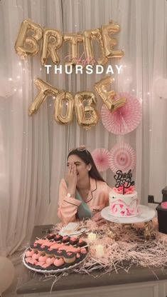 a woman sitting in front of a table filled with cakes and cupcakes