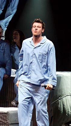 a man in blue pajamas standing on stage with his hands behind his back as he holds a remote control