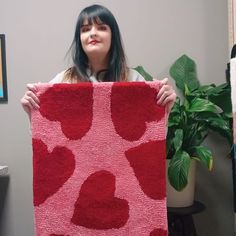 a woman holding up a red rug with hearts on it in front of a potted plant