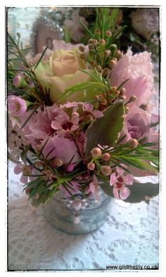 a glass vase filled with pink flowers on top of a white table covered in lace