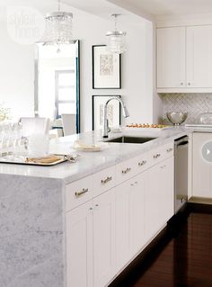 a kitchen with white cabinets and marble counter tops, along with an island in the middle