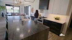 a woman standing in the middle of a kitchen with an island counter and black cabinets