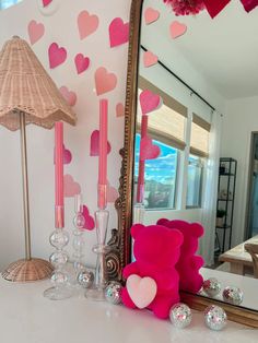 a pink teddy bear sitting on top of a table next to a mirror and candles